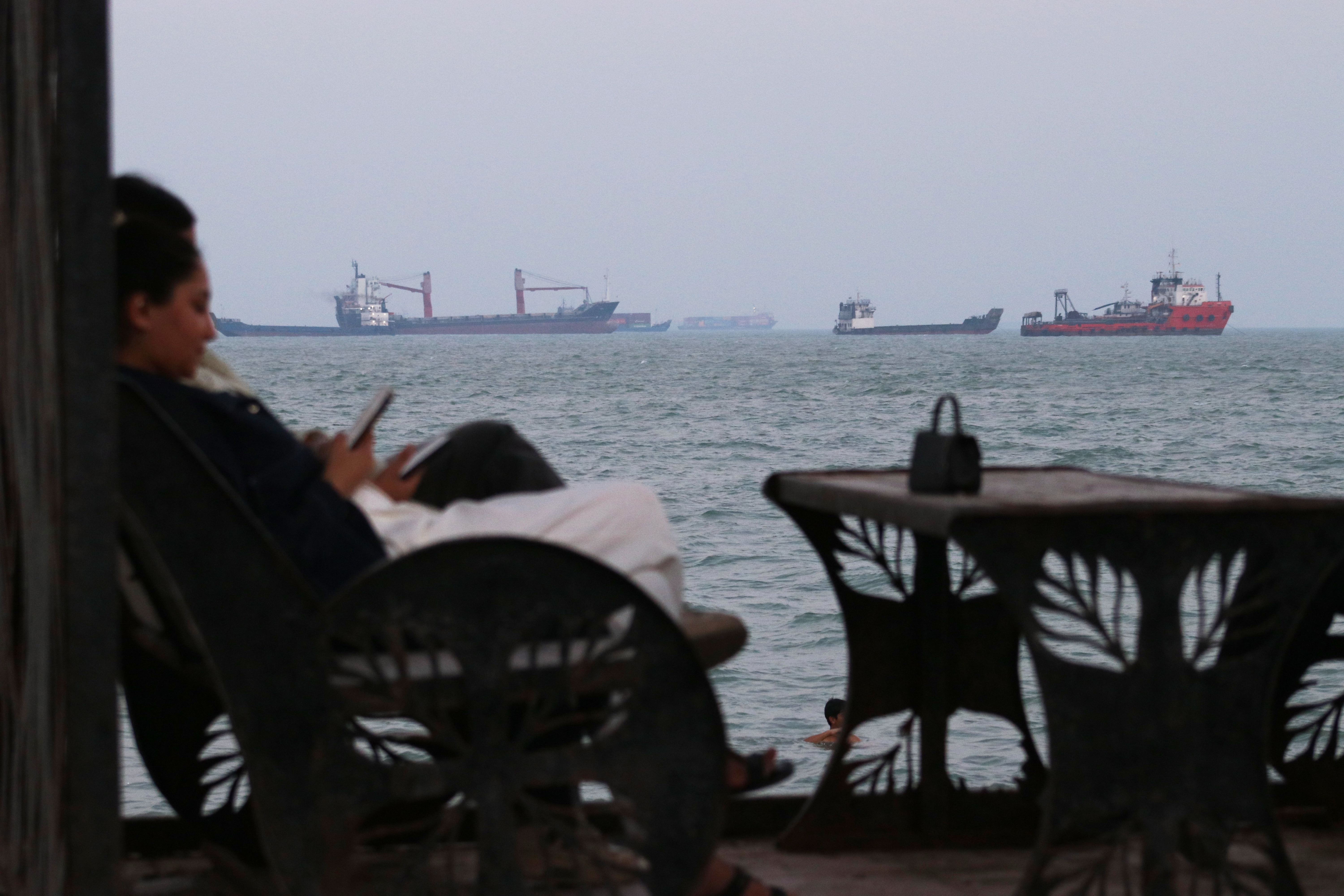 Residents check their cellphones as they sit at a cafe overlooking commercial vessels anchored in the Strait of Hormuz, off Bandar Abbas, Iran, Sunday, July 12, 2026.