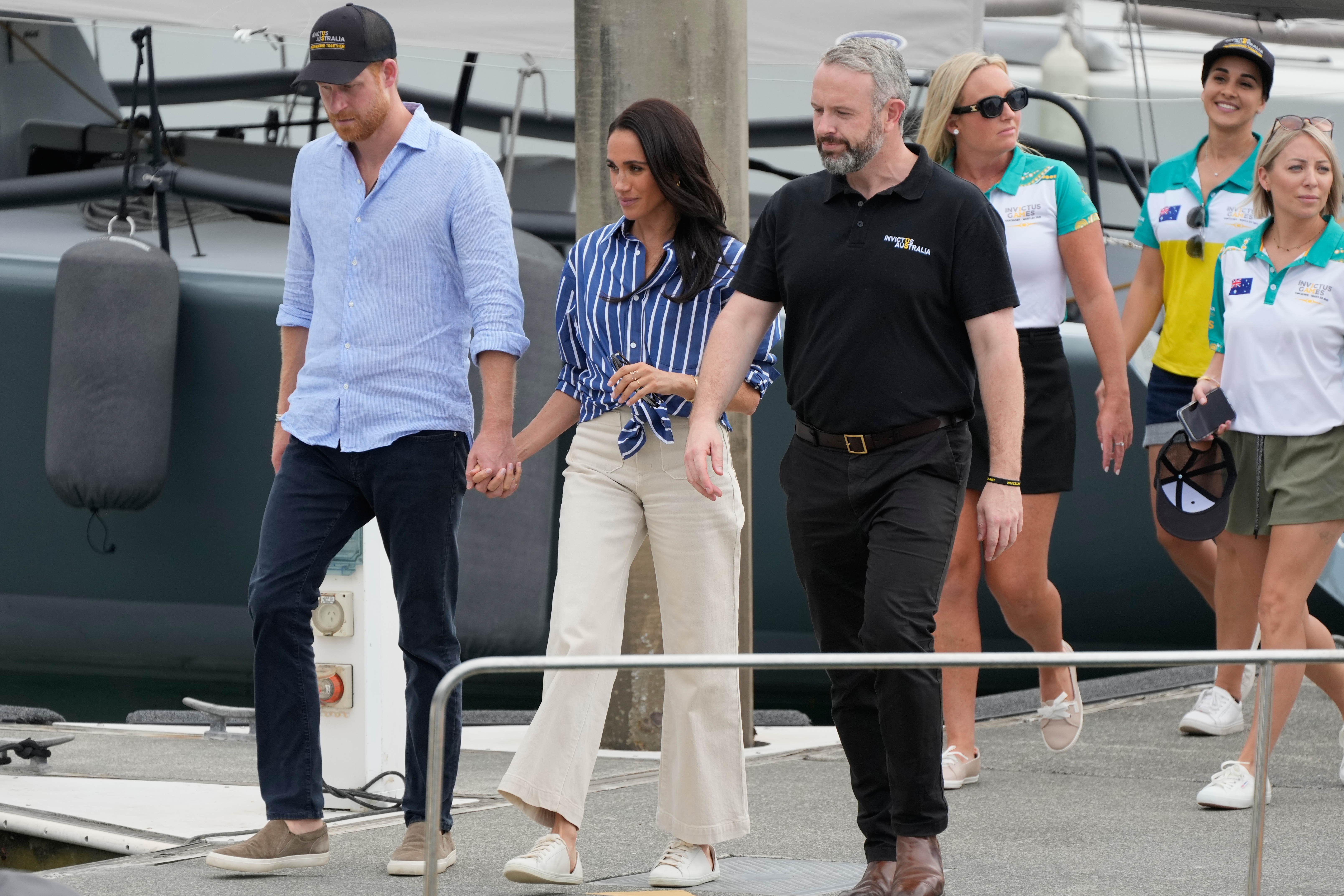 Prince Harry, left, and his wife Meghan, the Duke and Duchess of Sussex, arrive at a dock after sailing on the harbor in Sydney