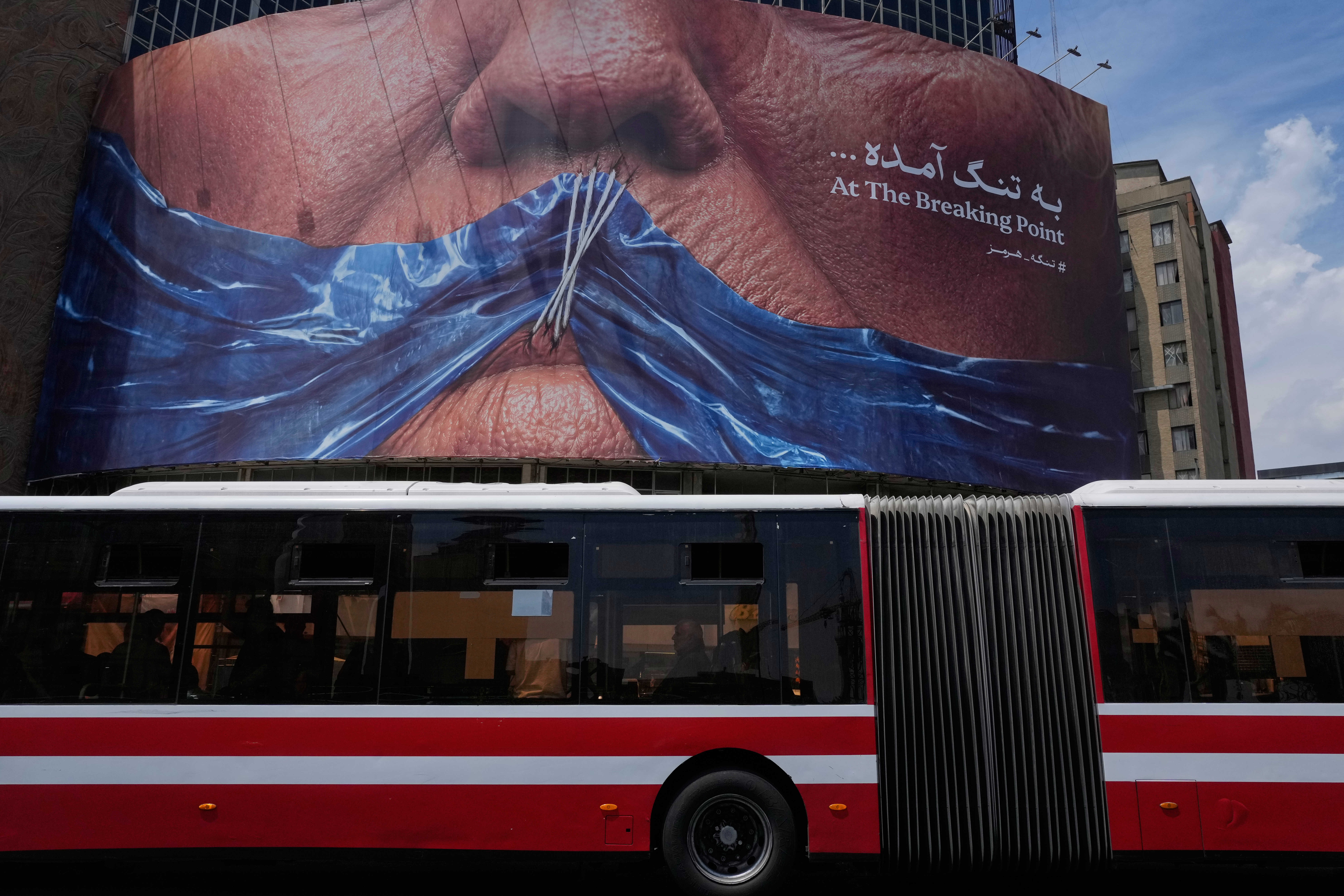 A public bus drives past a billboard with graphic showing Strait of Hormuz and sewn lips of US President Donald Trump in a square in downtown Tehran, Iran, Saturday, May 2, 2026.