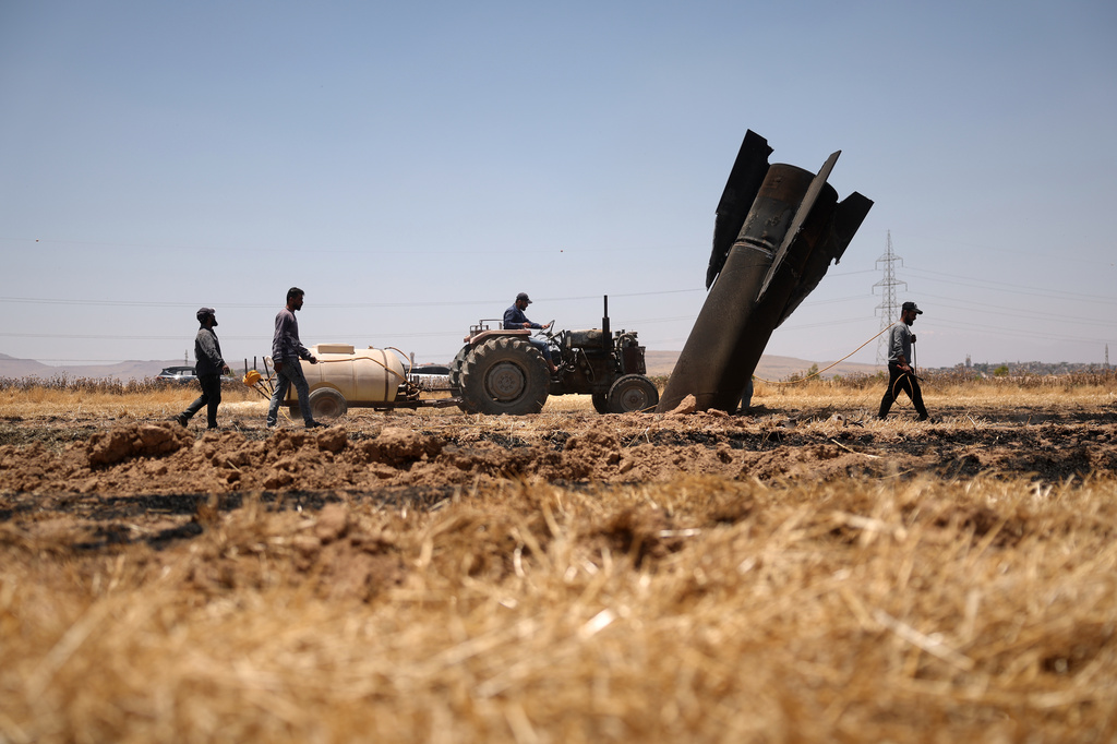 Farmers spray water in a burned agricultural field next to a projectile near the town of Najha, Syria, Monday, June 8, 2026.