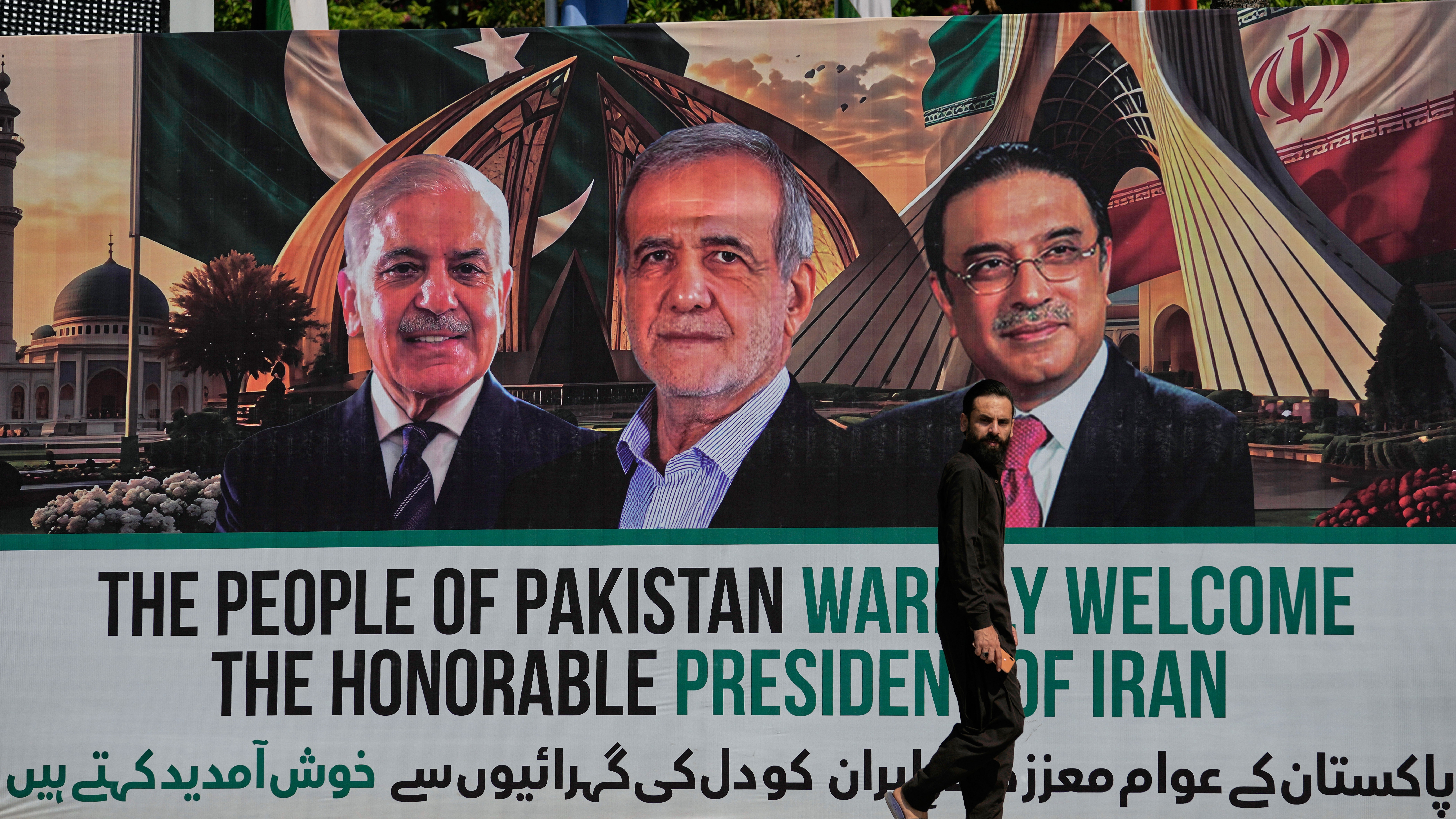 A man walks past a welcoming billboard featuring Iranian President Masoud Pezeshkian, center, with Pakistan President Asif Ali Zardari, right, and Shehbaz Sharif along a roadside in Islamabad, Pakistan.