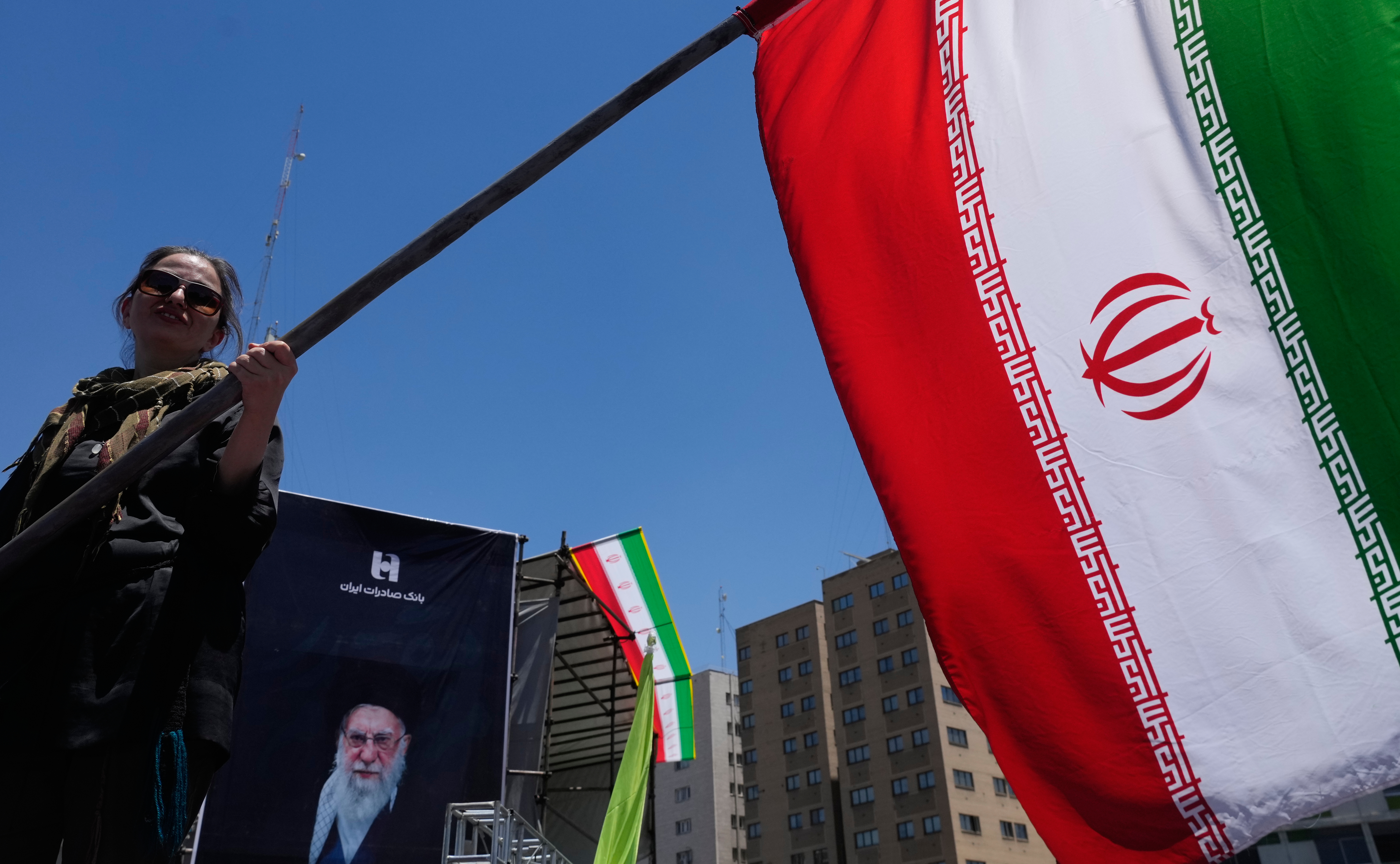 A woman waves an Iranian flag during a pro-government campaign as a portrait of the slain Supreme Leader Ayatollah Ali Khamenei.