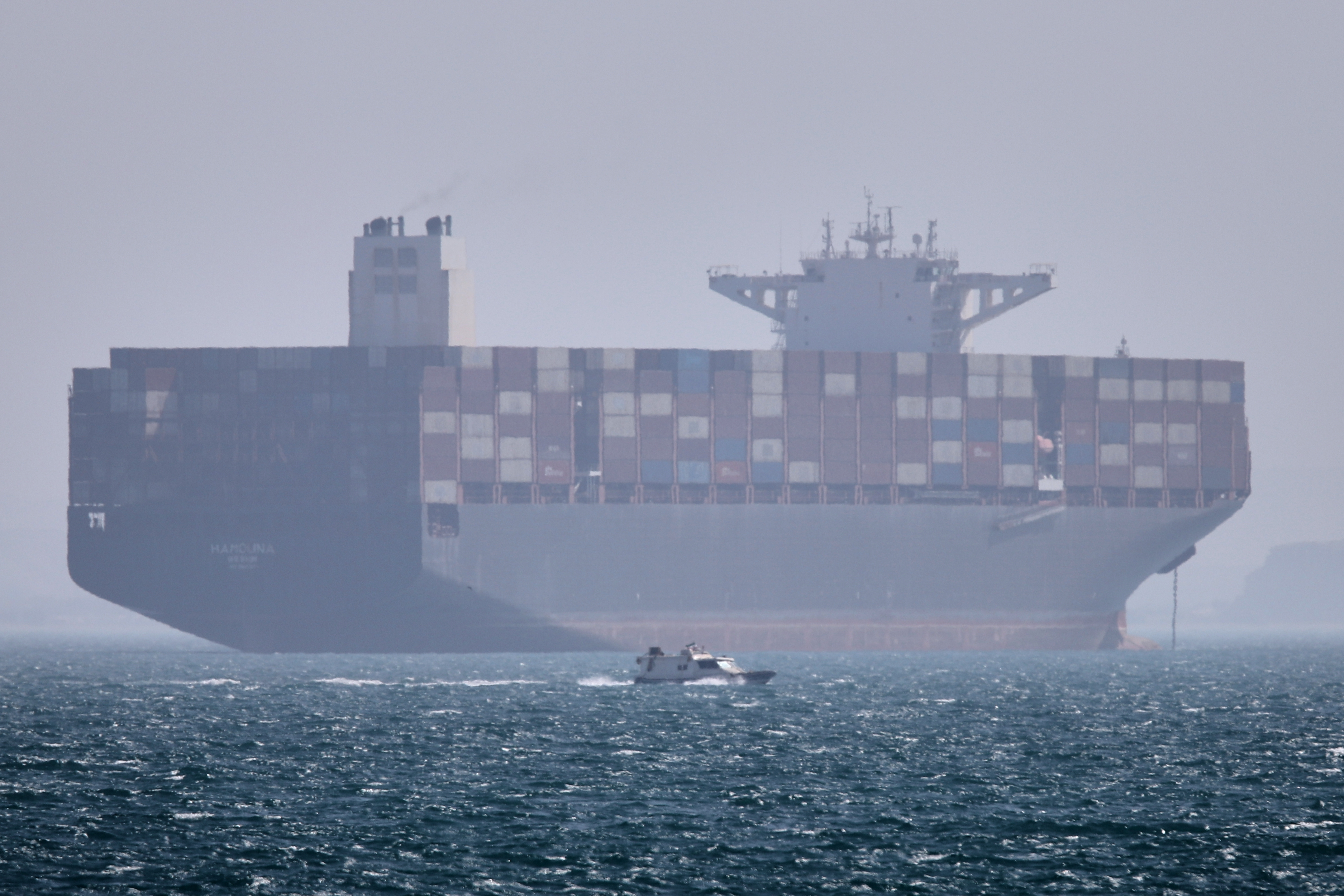 A container ship sits at anchor as a small motorboat passes in the foreground in the Strait of Hormuz off Bandar Abbas, Iran, Saturday, May 2, 2026. 