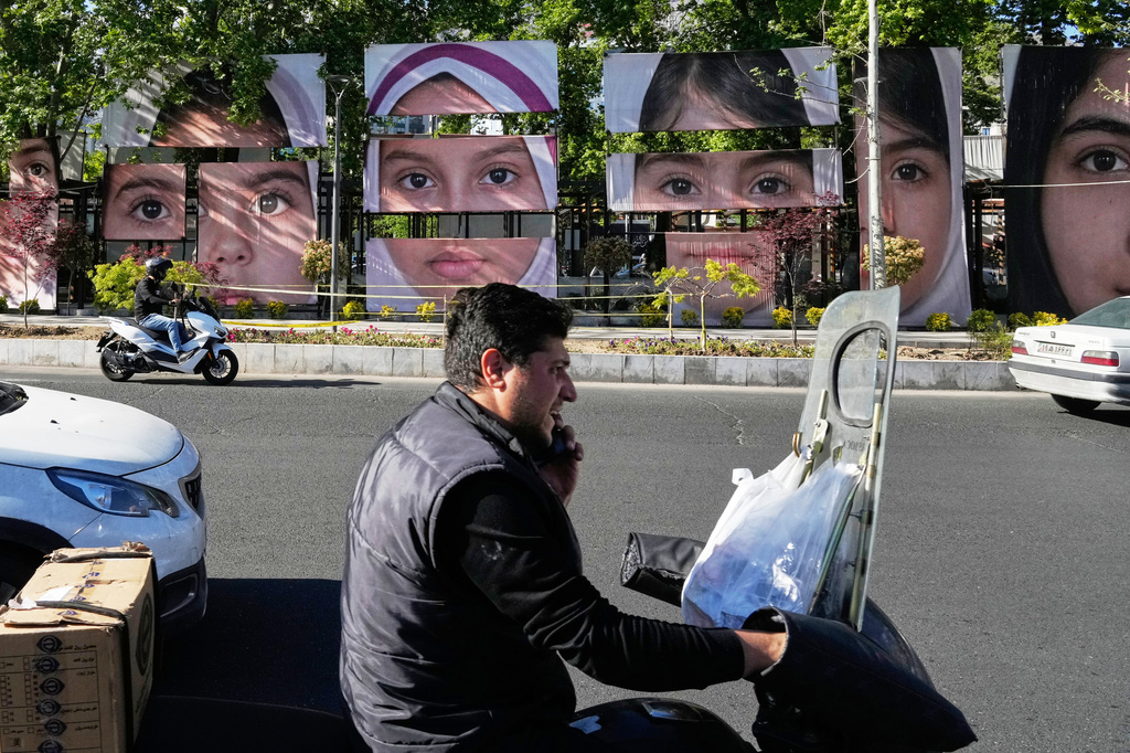 Vehicles drive past banners showing portraits of the school children who were killed during a strike on a school in southern town of Minab