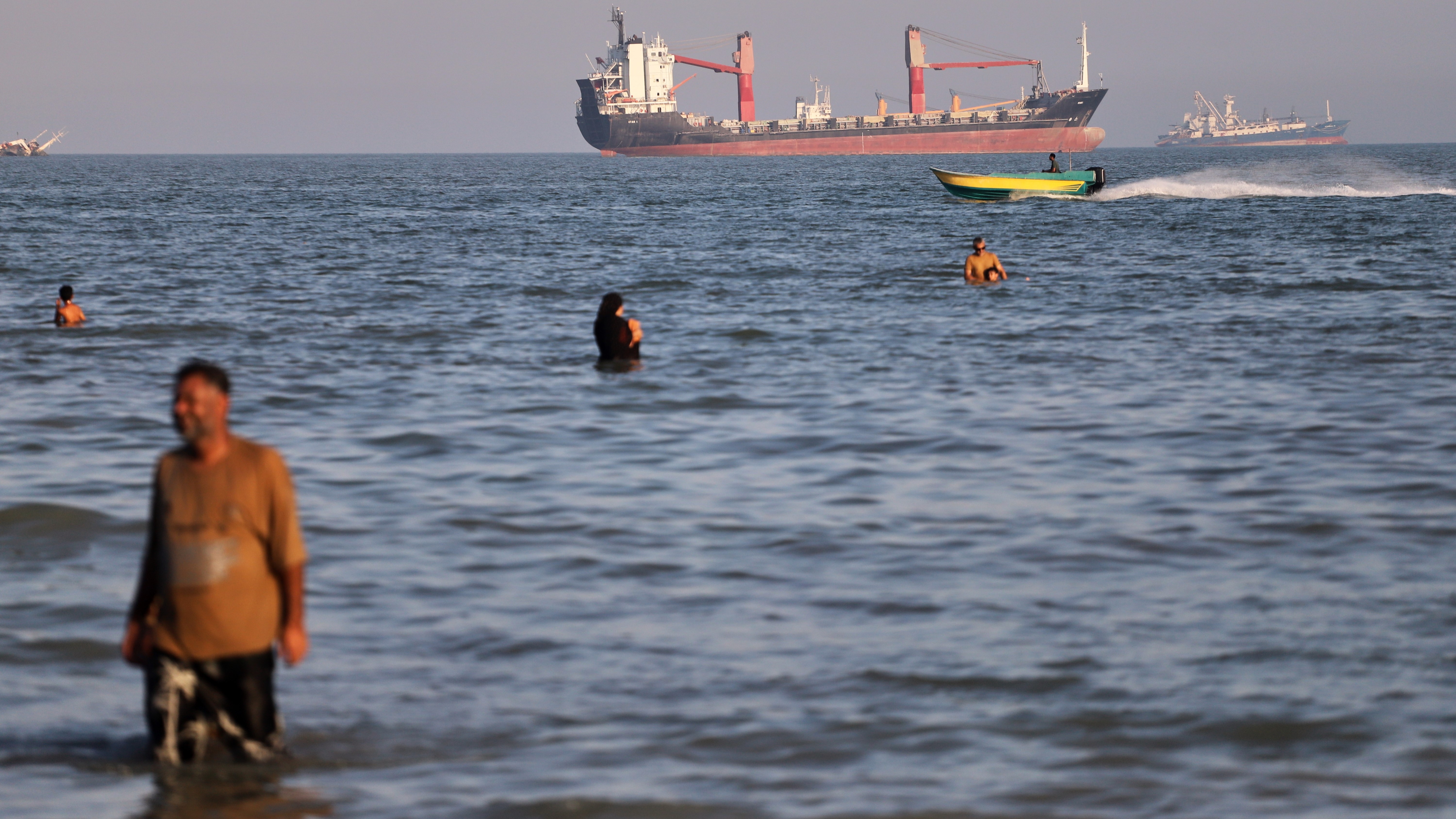 Residents swim in the waters of the Strait of Hormuz as a small motorboat passes cargo ships and other commercial vessels offshore near Bandar Abbas, Iran.