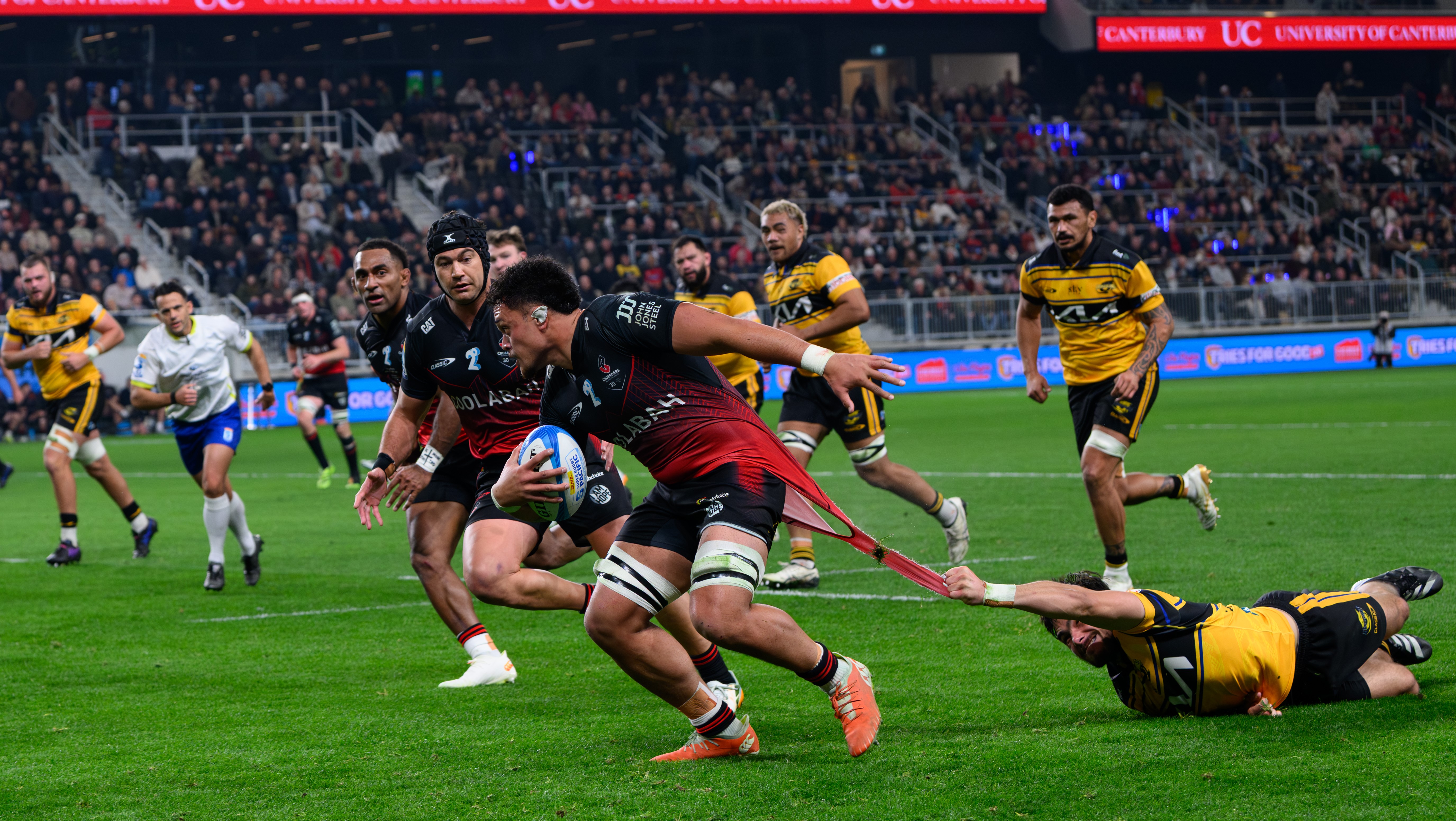 Crusaders loose forward Christian Lio-Willie has the shirt ripped off his back by a Hurricanes defender at Te Kaha.
