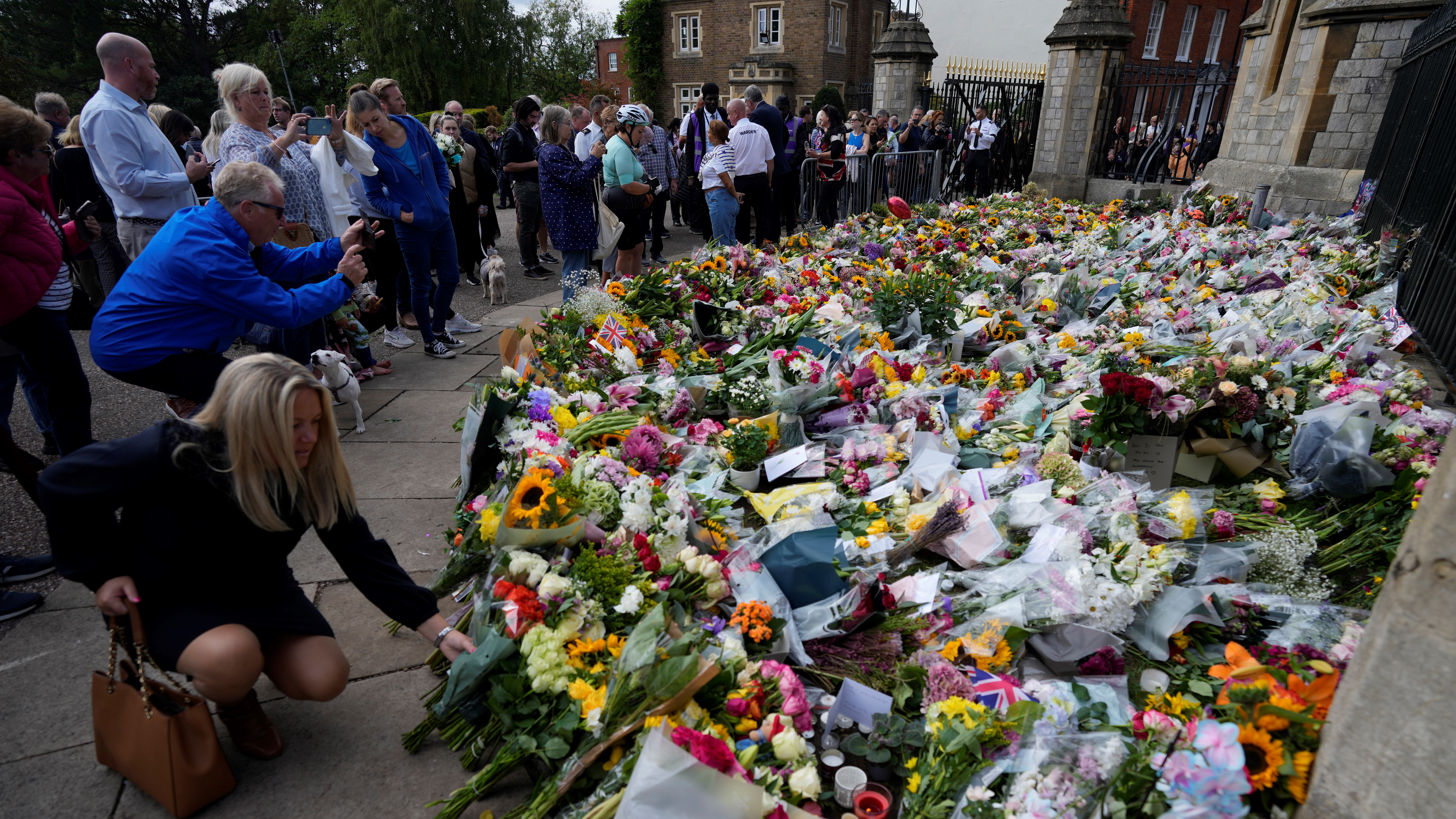 A woman places a flower with other floral tributes to Queen Elizabeth II outside the gates of Windsor Castle
