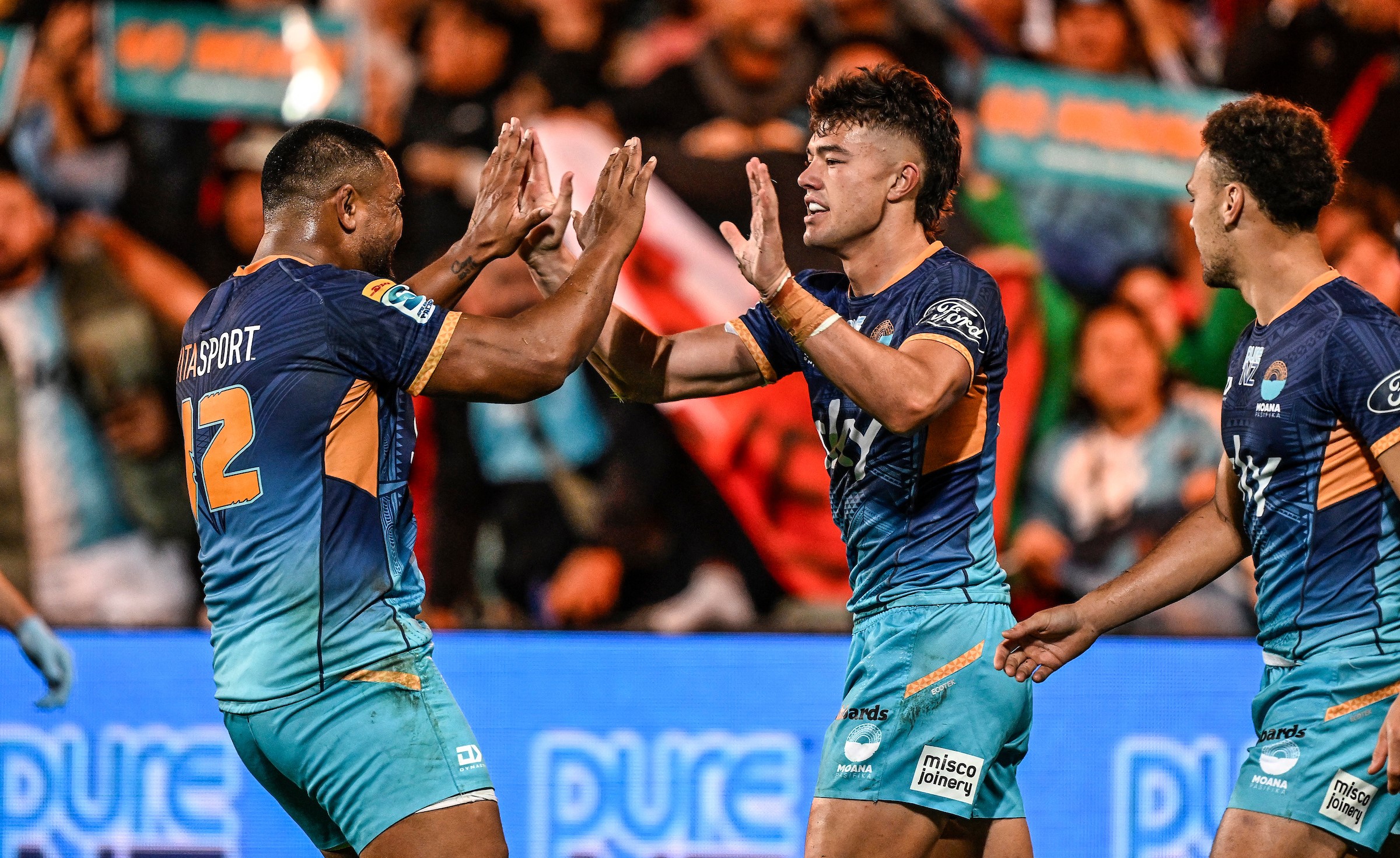 Moana Pasifika wing Kyren Taumoefolau celebrates one of his three tries with midfielder Julian Savea, left.