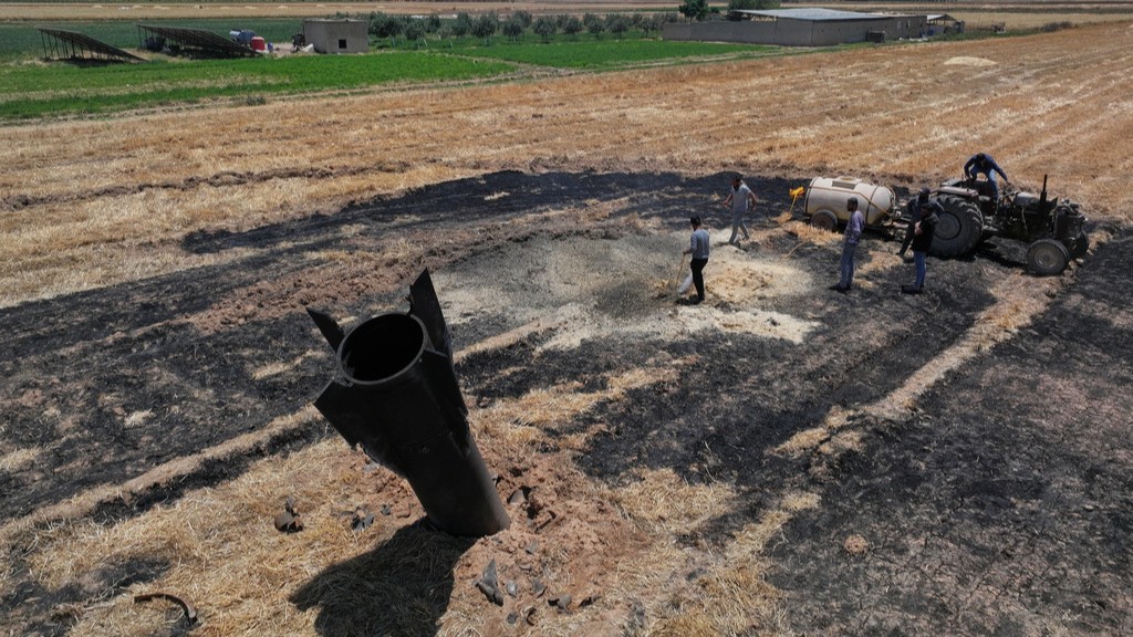Farmers spray water in a burned agricultural field next to a projectile near the town of Najha, Syria, Monday, June 8, 2026.