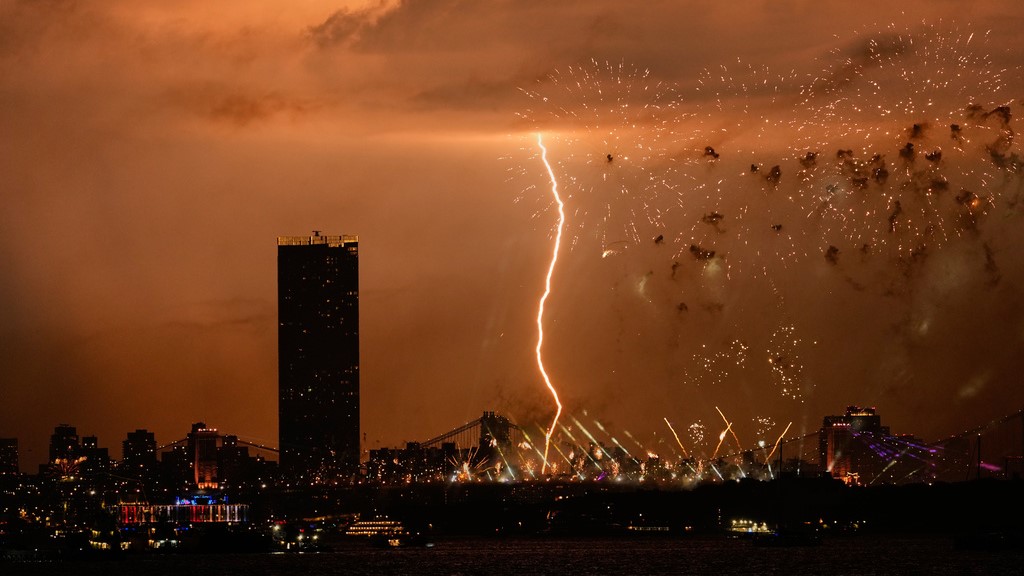 A bolt of lighting strikes as fireworks are set off of the Brooklyn Bridge, as seen from Bayonne, New Jersey.