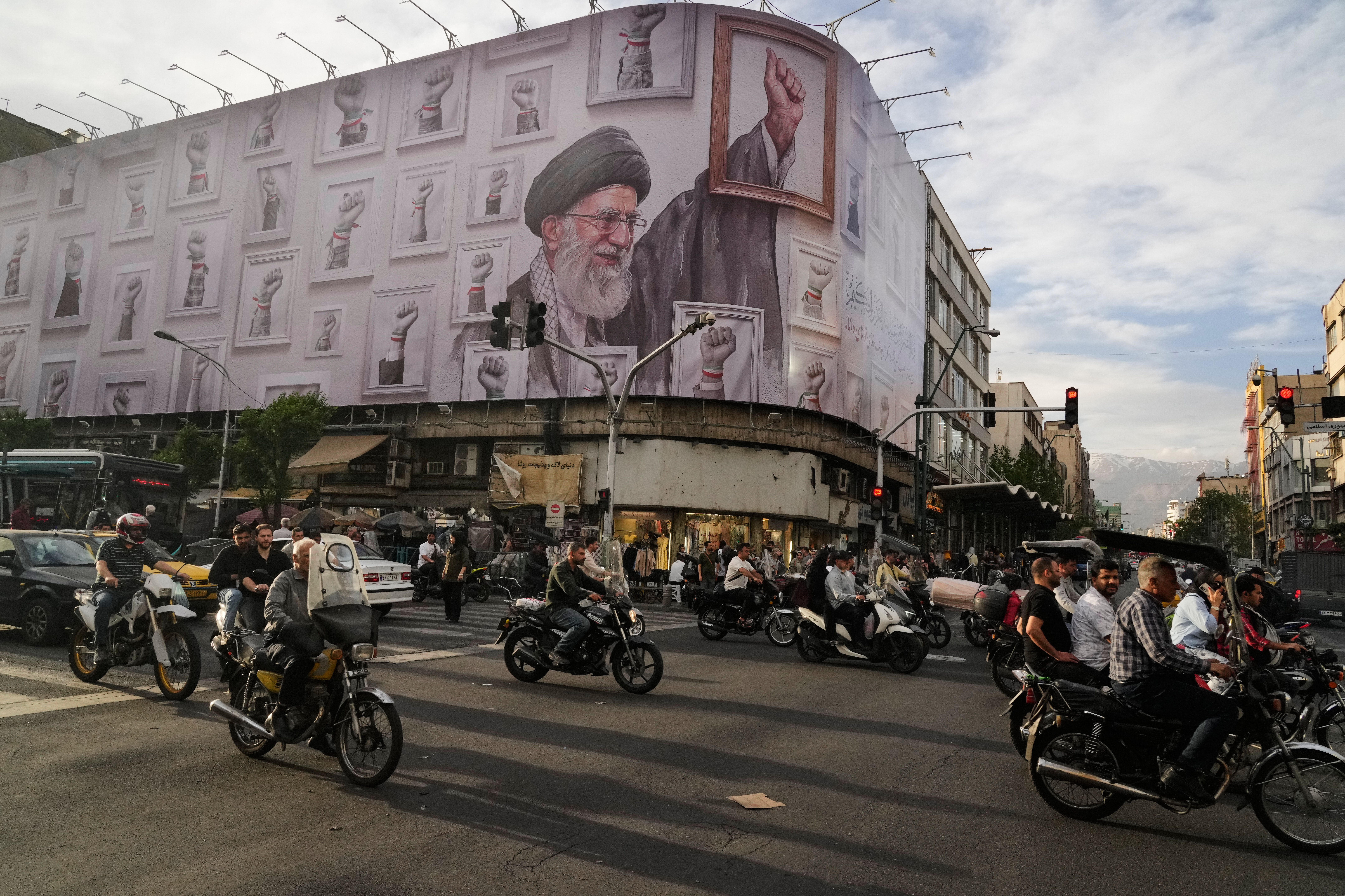 Motorbikes drive past a billboard with graphic showing the late Iranian Supreme Leader Ayatollah Ali Khamenei. 