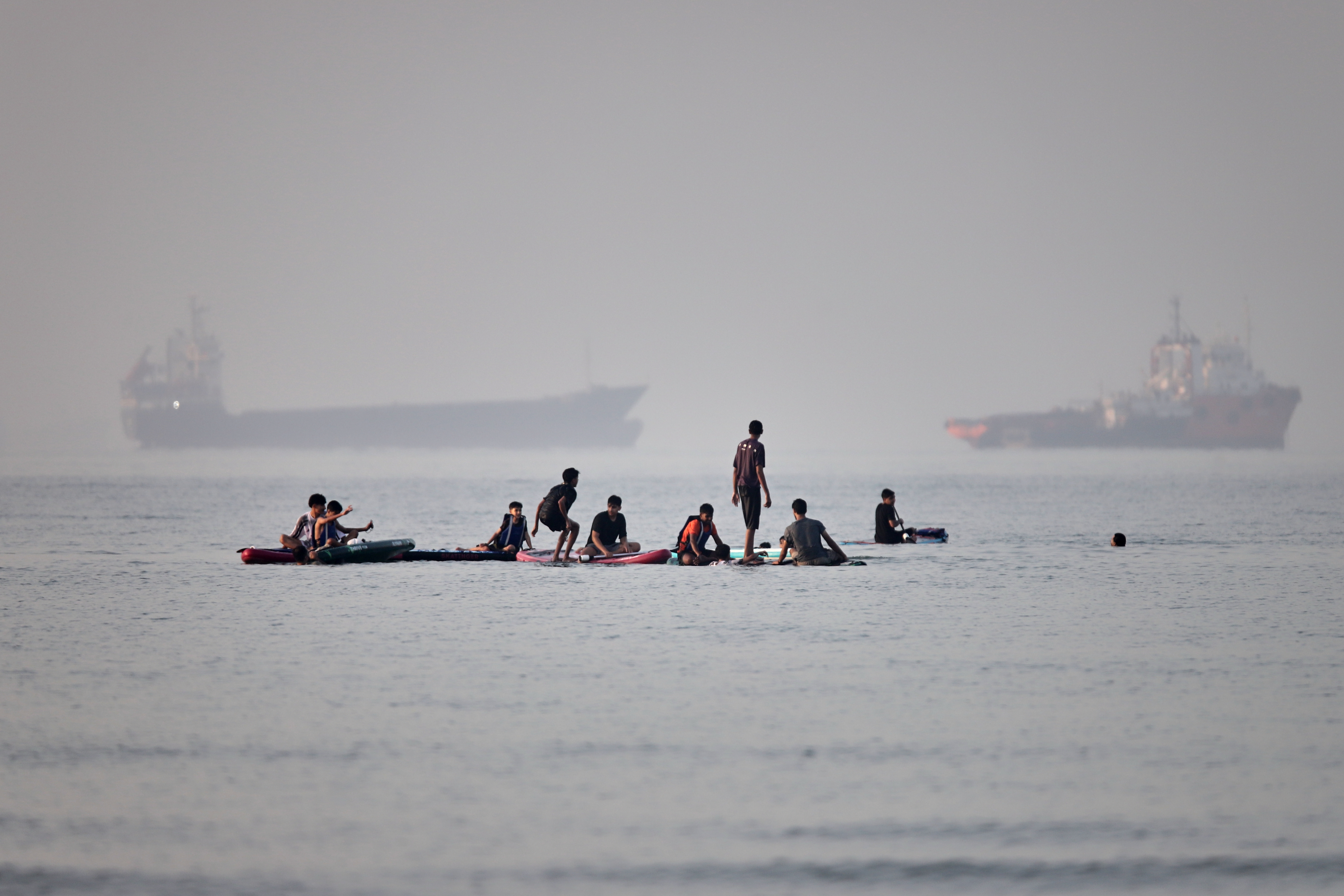 People gather on paddleboards in shallow water as cargo and service vessels are anchored in the Strait of Hormuz off Bandar Abbas, Iran, Monday, June 1, 2026.